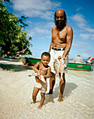 Boy and grandpa getting fish from the fisherman on the beach, Reunion, La Digue, La Digue and Inner Islands, Republic of Seychelles, Indian Ocean