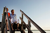 Couple sitting on a jetty at Lake Starnberg, Bavaria, Germany