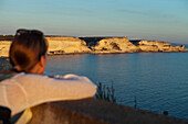 Woman gazes out over the limestone cliffs east of Bonifacio and Sardinia on the horizon, Corsica, France