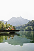 Zwei Mädchen sitzen auf einem Steg am Schwansee, Schwangau, Allgäu, Bayern, Deutschland