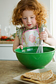 Little girl mixing ingredients in a bowl with a whisk