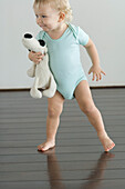 Little boy holding stuffed dog, standing on wooden floor