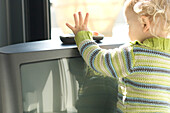 Little boy taking TV remote control, rear view