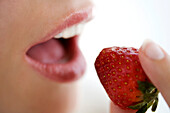 Young woman face eating a strawberry, close-up, indoors, studio