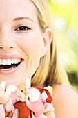 Portrait of a young  blond woman smiling, holding petals, outdoors