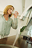Woman drinking glass of water, tap in foreground