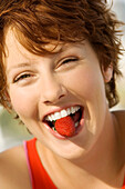 Portrait of a young woman holding strawberry between her teeth