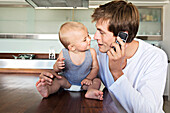 Young man phoning, embracing baby