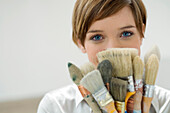 Portrait of a young woman holding paintbrushes in front of her face