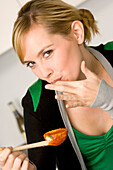 Portrait of a young woman tasting tomato sauce with her finger