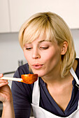 Close-up of a young woman blowing tomato sauce on a wooden spoon