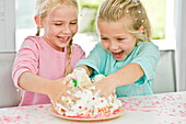 Two girls playfully inserting their hands in a birthday cake