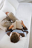 Boy lying on a couch and reading a book