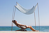 Woman resting in a deck chair under a canopy