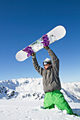 Young man holding his snowboard above his head