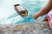 Low section view of a girl sitting at edge of swimming pool with toy boat in water