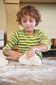 Cute little boy kneading dough at kitchen