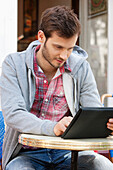 Man sitting at a sidewalk cafe using a digital tablet, Paris, Ile-de-France, France