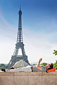 Man lying on a stone wall with the Eiffel Tower in the background, Paris, Ile-de-France, France