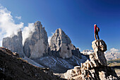 Woman standing on a rock tower in front of the three peaks, Tre Cime di Lavaredo, Sexten Dolomites, Dolomites, UNESCO World Heritage Site, South Tyrol, Italy