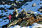 Woman walking through snow covered rocks and cairns, Peterskoepfl, Zillertal range, Zillertal, Tyrol, Austria