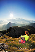 Woman sitting at the summit and looking towards the Inn valley and the Kaiser mountain range, Brunnstein, Bavarian Prealps, Upper Bavaria, Bavaria, Germany