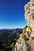 Frau quert auf ausgesetztem Weg durch Felswand, Brünnstein, Bayerische Voralpen, Oberbayern, Bayern, Deutschland
