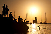 People watching the sunset on rocks beside Benirras beach, Ibiza, Spain.