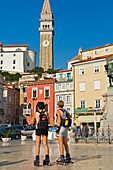 In-line skating women tourists at Tartini Square, The medieval centre of Piran, Slovenia, with St. George's Cathedral in the background.