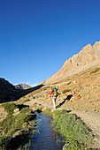 Woman hiking along a stream, Sirsir La, between Honupatta and Photoksar, Zanskar Range Traverse, Zanskar Range, Zanskar, Ladakh, Jammu and Kashmir, India