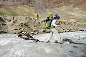 Frau überquert Bach auf Steinen, Photoksar, Großer Zanskar Trek, Zanskargebirge, Zanskar, Ladakh, Jammu und Kashmir, Indien