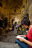 Woman reading guidebook beside stalls in covered gateway in Khan El Khalili, Cairo, Egypt