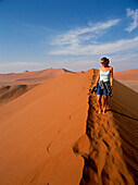 Woman walking on top of sand dune in the desert, Sossusviel, Namibia
