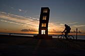Silhouette of cyclist passing sculpture, Barcelona, Catalonia, Spain