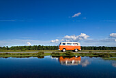 Orange campervan driving past pond, New Forest, Hampshire