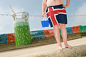 Lower half of man with bucket and union jack shorts in front of Bathing Beauties beach huts: Come up and see me, Mablethorpe, Lincolnshire, UK