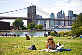 Girl lying in park, Dumbo, Brooklyn Bridge in background, Brooklyn, New York, USA