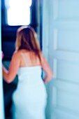 Blurry back view of a woman in a white dress going in a doorway inside of a home