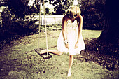 Blonde Woman in White Dress Bending Over While Resting One Foot on Swing