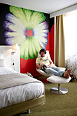 Mann sitzt in einem Hotelzimmer, Blumenfresko im Hintergrund, Hotel Bloom, Brüssel, Belgien