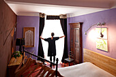 Woman opening curtains, Bedroom with double bed, B and B Chambre Avec Vue, Luberon, France
