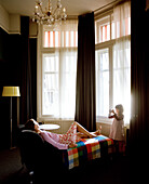 Girl shoot a photograph of mother lying on a chaiselounge in a hotel room, Rotterdam, Netherlands