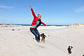 Leba Dunes, young woman jumping into the dunes, view towards the sea, UNESCO World Biosphere Reserve, Slowinski National Park, Polish Baltic Sea coast, MR, Leba, Pomeranian, Poland