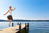 Mädchen springt auf Bootssteg am Starnberger See, Oberbayern, Deutschland