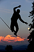 Junger Mann balanciert über eine Longline bei Sonnenuntergang, Auerberg, Bayern, Deutschland, Europa
