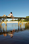 Teenage couple on jetty. Teenage couple on jetty, she is resting her head in his lap. They are reflected in the water.