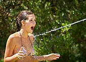 Teenage girl being sprayed with water. Teenage girl in bikini being sprayed with water in garden.