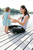Frau sitzt mit kleinem Kind auf einem Holzsteg, Alte Donau, Wien, Österreich