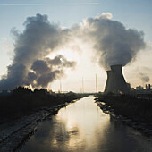 Oil refinery buildings silhouetted against the sky.  Vapour. Smoke rising. Canal waterway. Aircraft flying high overhead. Vapour trail across the sky. Grangemouth, Scotland, UK., Oil refinery, Grangemouth, Scotland.