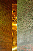 Glimpse of the reclining Buddha at Wat Pho temple. Head and arm. Seen through a gap in the mosaic covered pillars. Gilded statue., Bangkok, Thailand. Statue of a reclining Golden Buddha